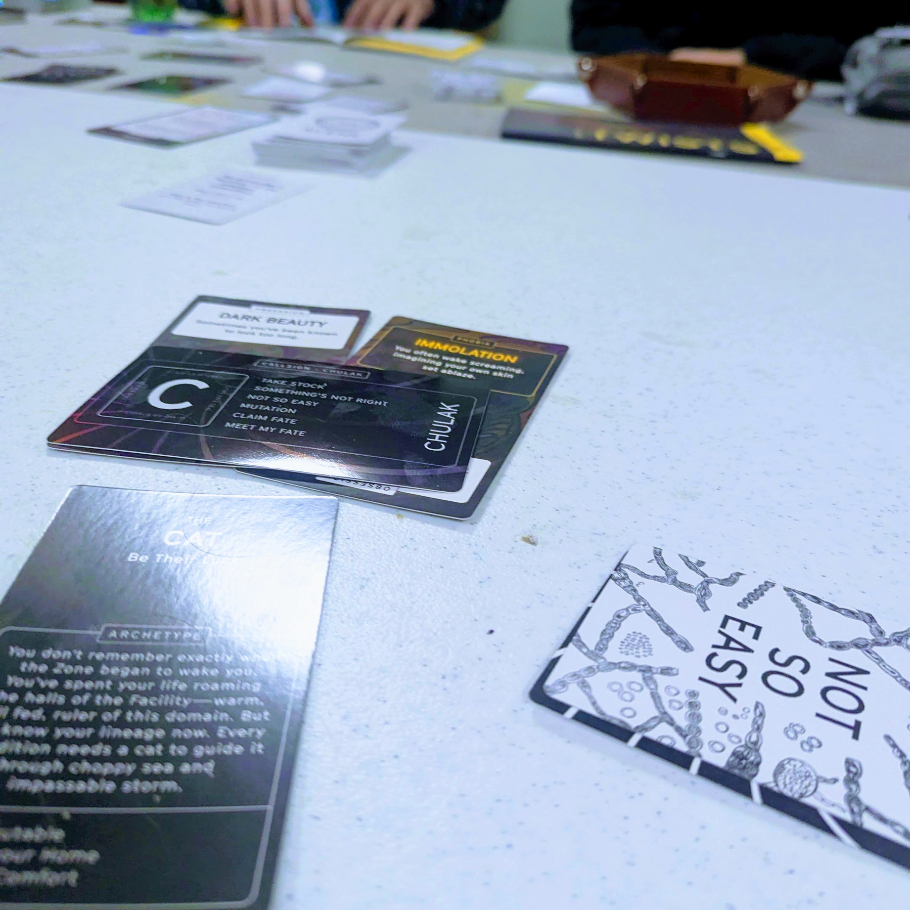 People are playing a card game (The Zone) with various cards spread out on a table.
